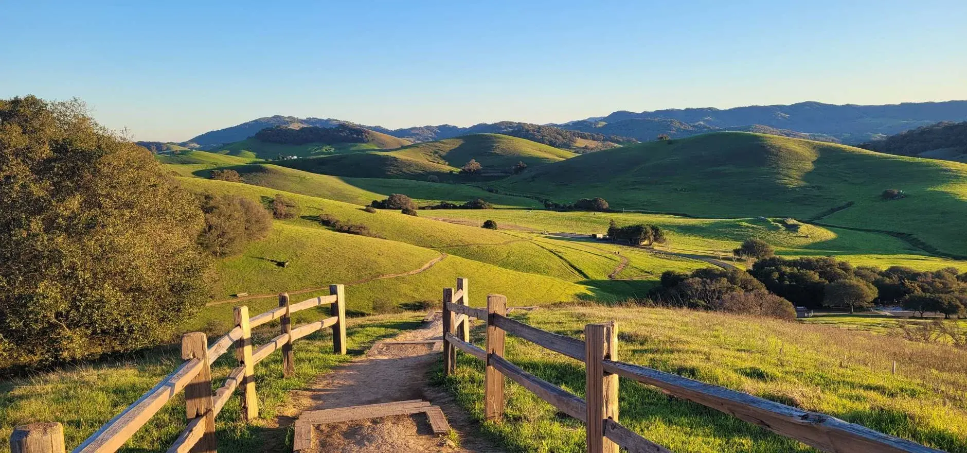 Trail between wooden fences overlooking green hills