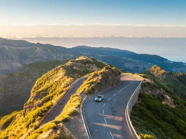 Car on winding mountain road above clouds
